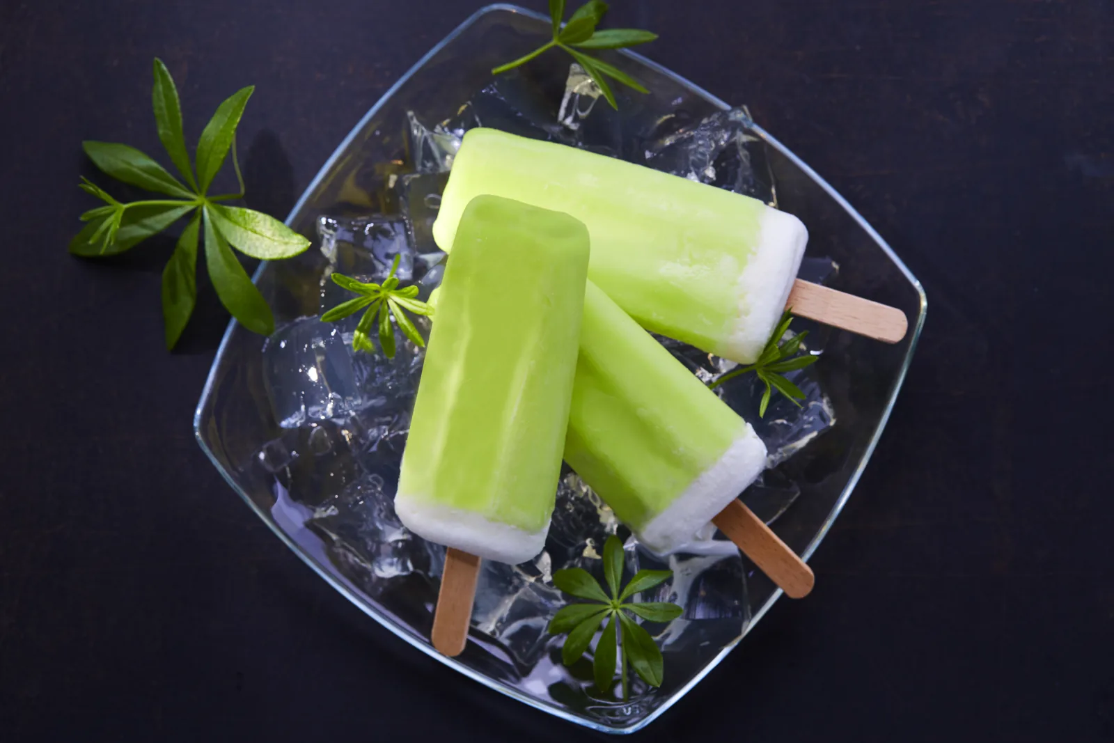 Waldmeister-Eis am Stiel auf Eisw&uuml;rfeln mit gr&uuml;nen Bl&auml;ttern