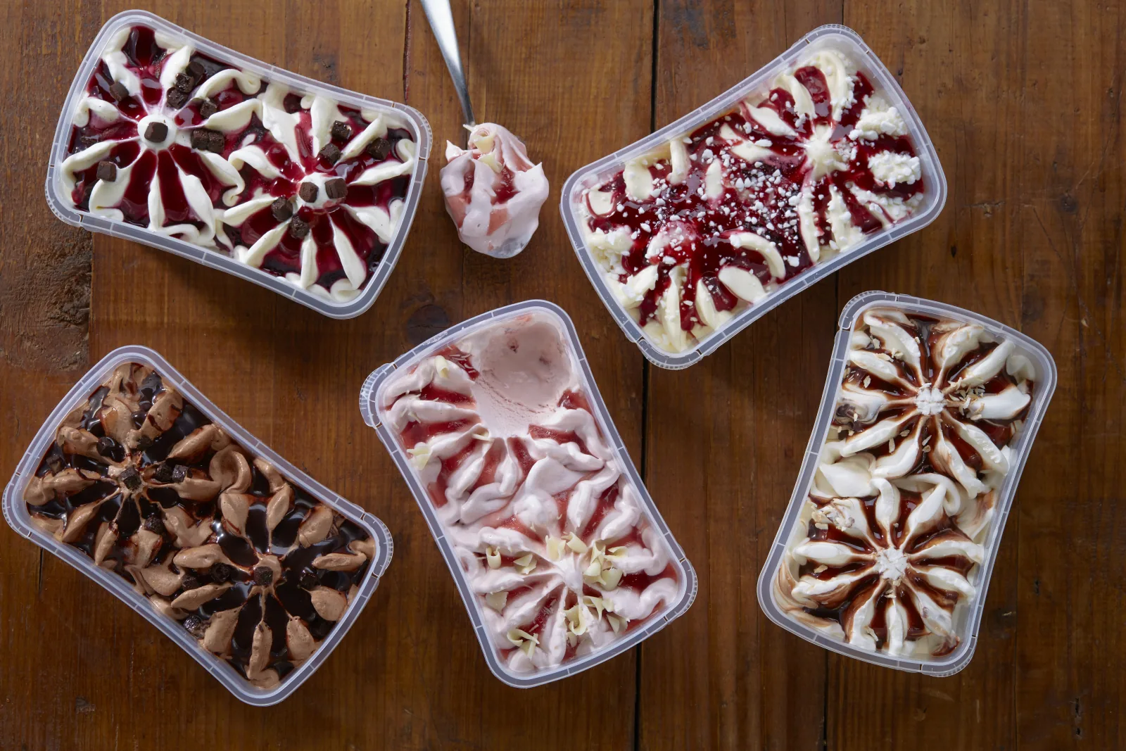 F&uuml;nf Eisdosen mit unterschiedlichen Fruchtsaucen von oben fotografiert